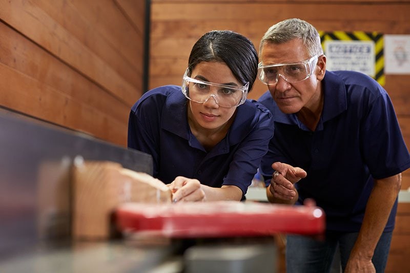 female learning to use table saw with instructor