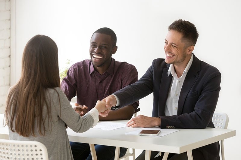 two men smiling and shaking hands with woman sitting at table